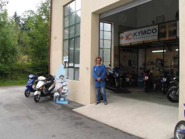 Elektroroller Händler nahe Salzburg
Von links nach rechts: E-Max S in blau, E-Max in grau, und ein Pappendeckel mit aufgemalten Elektromoped, Herr Deinlein und einige Kymco 4 Takt Mopeds in der Werkstatt.